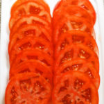 Our thinly sliced fresh red tomatoes on the cutting board are awaiting the assembly of the sandwich