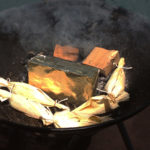 The grill has the Smokinlicious Smoker Wood Chunks around the brick and the snapper wrapped in corn husk on the grill